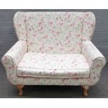 A modern child's wing back sofa, on squat cabriole supports with floral and bird print upholstery,