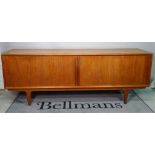 A mid-20th century teak low sideboard, with sliding doors on tapering supports,