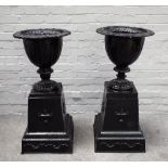 A near pair of black painted cast iron garden urns, on urn and swag moulded square bases,