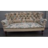A late 19th / early 20th century tub back two seat sofa, on turned mahogany supports,