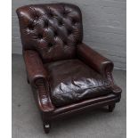 A brown leather button back upholstered easy armchair, on turned supports, 80cm wide x 85cm high.