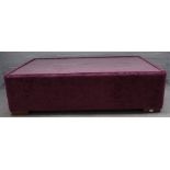 A large square plum coloured upholstered coffee table, with inset glass top on block supports,