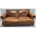 A 20th century brown leather upholstered sofa, with roll over arms on turned supports,
