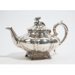 A Victorian silver teapot, of compressed panelled form, the hinged lid having a flower finial,