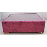 A large square plum coloured upholstered coffee table, with inset glass top on block supports,