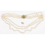 A three row necklace of graduated cultured pearls, on a gold and green gem set clasp,