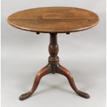 A George III oak tea table, the circular tilt-top, on a baluster turned pillar and tripod base,