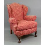 A reproduction George I style upholstered wing back armchair, on leafy scroll carved cabriole legs.