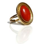 A gold mounted oval coral ring, the oval coral mounted within a textured border,