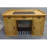 An early 20th century pine writing desk with three frieze drawers over cupboard doors,