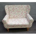 A modern child's wing back sofa, on squat cabriole supports with floral and bird print upholstery,