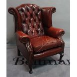 A George III style leather upholstered wingback armchair on cabriole supports and pad feet,