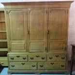 A late George III pine triple wardrobe with three paneled doors over an arrangement of five drawers,