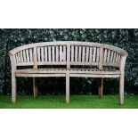 A teak semi-elliptic garden bench of slatted construction on block supports,
