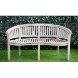 A teak semi-elliptic garden bench of slatted construction on block supports,
