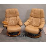 A pair of contemporary tan leather upholstered swivel armchairs with reclining stools,