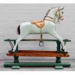 An early 20th century green painted wooden rocking horse with a tan saddle and glass eyes,