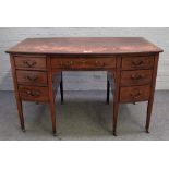 An Edwardian tulip wood banded mahogany bowfront writing desk with seven drawers about the knee on