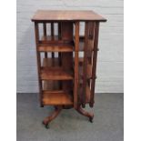 An Arts & Crafts walnut square four tier revolving bookcase, on three downswept supports,