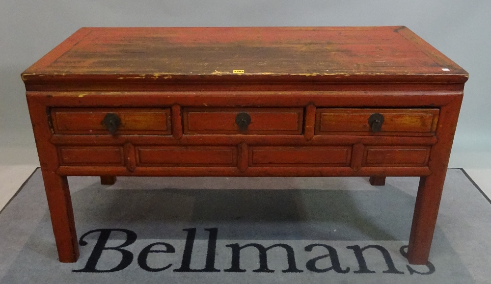 An early 20th century red painted Chinese low side table with three short drawers on block supports,