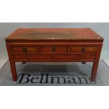 An early 20th century red painted Chinese low side table with three short drawers on block supports,