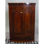A 19th century mahogany hanging corner cupboard with moulded arch doors and single drawer base,