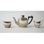 A late Victorian silver composite three piece tea set, comprising; a teapot with black fittings,