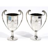 A pair of silver twin handled trophy cups, each of multi-sided form with foliate capped handles,