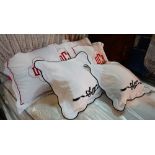 A set of four white pillows with red trim and initials 'DMC' to the centre,