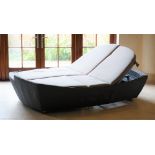 A grey woven day bed lounger for two persons, with adjustable back and footrests and loose cushions.