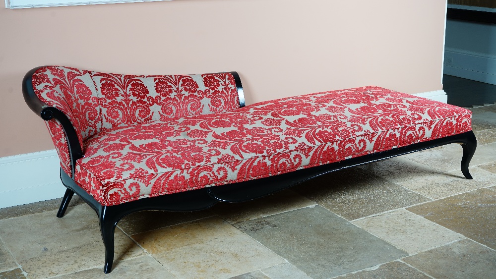 A large ebonised chaise longue, with shaped back and stuff-over seat, on cabriole legs,