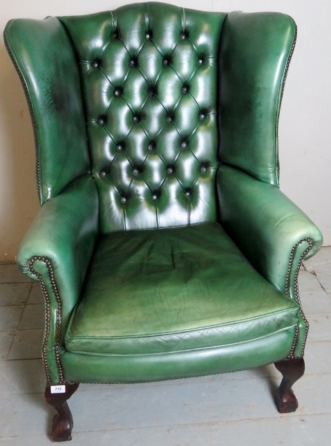 A 20th century green leather deep buttoned winged armchair, terminating on ball and claw feet,