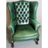 A 20th century green leather deep buttoned winged armchair, terminating on ball and claw feet,