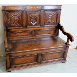 A 20th Century oak monk's bench with carved panels to back over a lift up seat revealing internal