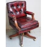 A 20th Century mahogany framed swivel office desk chair upholstered in a burgundy button backed