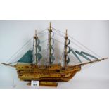 A large wooden scale model of a three masted sailing ship in full sail.