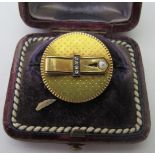A heavy 18ct gold circular brooch, with a belt design centre, inset with four diamonds and a pearl.