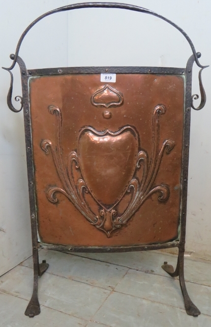 A decorative Art Nouveaux fire screen with an embossed copper panel inset in an ironwork frame.