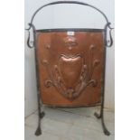 A decorative Art Nouveaux fire screen with an embossed copper panel inset in an ironwork frame.