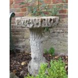 A concrete garden bird bath with a circular dished top over a column base modelled as a tree trunk.