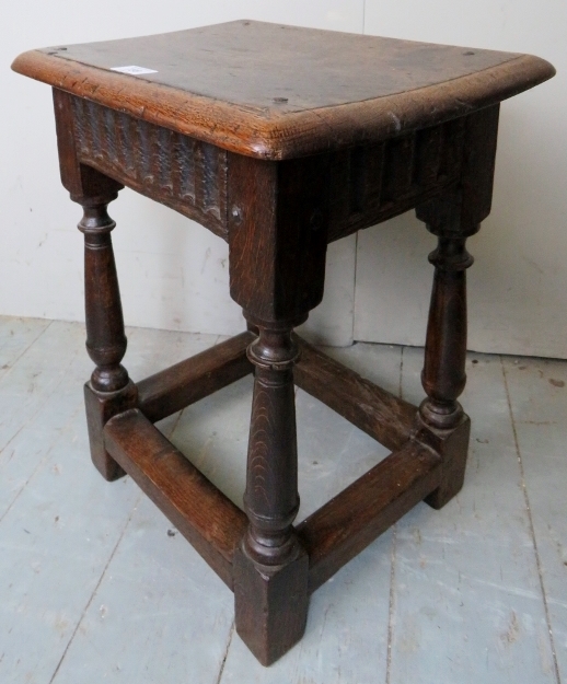 A 17th Century and later country oak joint stool with a carved linen fold frieze over turned