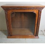 A carved oak bookcase / display cabinet with panelled sides and glazed door revealing two