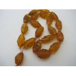 A honey coloured amber figural face carved prayer necklace.