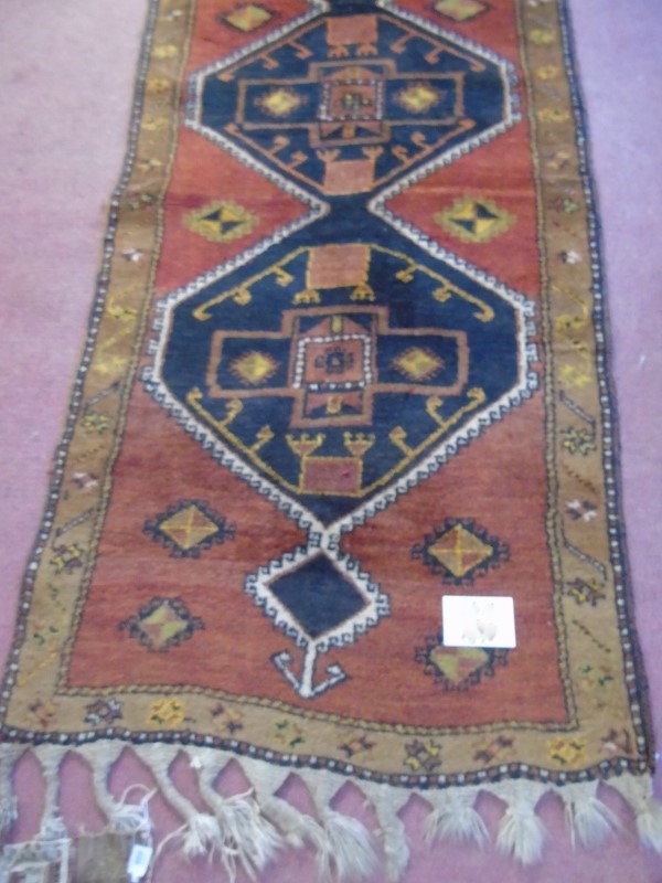 An early-mid 20's Turkish runner with repeated central motif on a red ground and tan border.