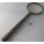 A large white metal magnifying glass. The graduated handle decorated with deity.
