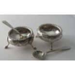 A pair of Victorian silver circular salts with embossed flower decoration on pad feet and a pair of