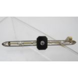 An Art Deco yellow metal bar brooch. Set with centre onyx inset with diamond and two seed pearls.