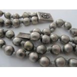 A vintage double row of white metal individually knotted beads, with white metal floral clasp.