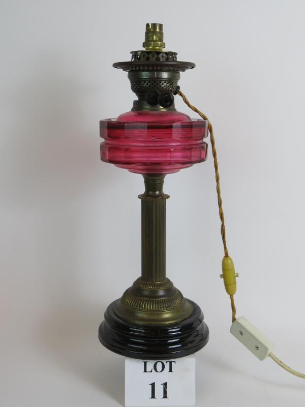 An antique Cranberry glass oil lamp later converted to electricity, with black porcelain base.