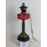 An antique Cranberry glass oil lamp later converted to electricity, with black porcelain base.